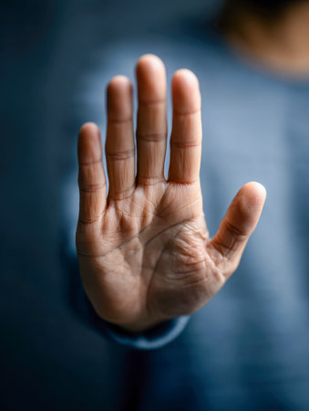 A warm-toned individual extends their palm directly toward the viewer, conveying a firm message of halt amid a gentle, softly lit setting and a smoothly blurred backの写真素材