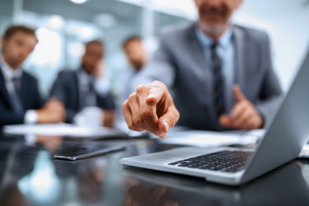 A professional male leader directs attention to key insights on a laptop, engaging team members in a collaborative discussion within a sleek, contemporary workspace.の写真素材