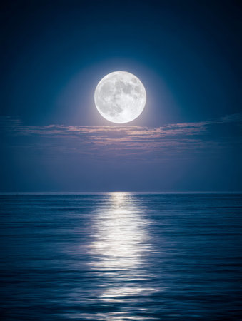 A radiant moon ascends above tranquil seas, its glow softly illuminating drifting clouds and casting a peaceful mirror image on the surface below.の写真素材