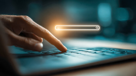 A user engages with a sleek laptop keyboard under dim lighting, illuminated by a luminous search bar suggesting rapid digital exploration during nighttime.の写真素材