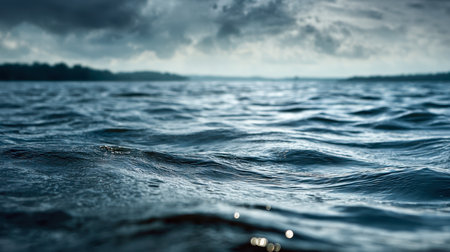 A somber lakeside scene featuring soft ripples on black water, framed by a turbulent sky hinting at an imminent storm and a powerful shift in weather.の写真素材