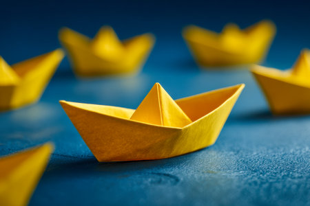 Vibrant yellow origami boats are artfully positioned on a rich blue textured background, with the central vessel highlighting unity and collaborative strength.の写真素材