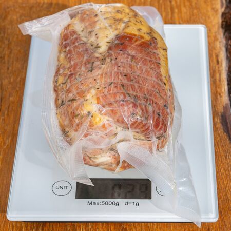 Pork ham in a sealed vacuum packaging on scales on a wooden table closeupの写真素材