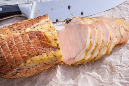 Fresh slices of pork ham on a white paper with black pepper and rosemary and knife on backgroundの写真素材