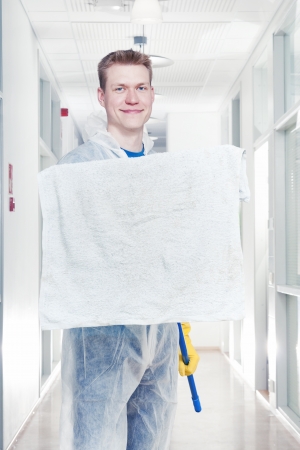 Man cleaning office wearing protective overalls, holding a mop towards camera, room for textの写真素材