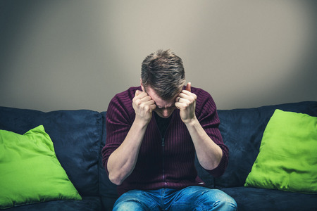 Man sitting on sofa looking painfulの写真素材