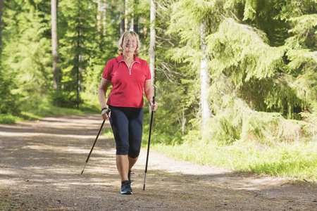 Nordic walking active senior woman working out in the forest and enjoying beautiful summer day. の写真素材