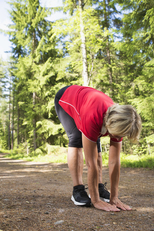 Athletic and flexible senior woman stretching in sportswear after exercise at jogging track. の写真素材
