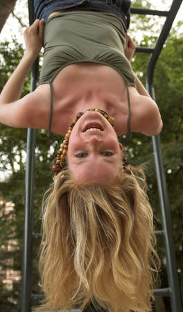 Blonde girl hanging upside down in an outdoor playgroundの写真素材