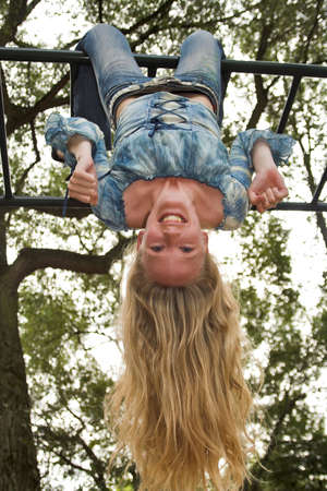 Blonde girl hanging upside down in an outdoor playgroundの写真素材