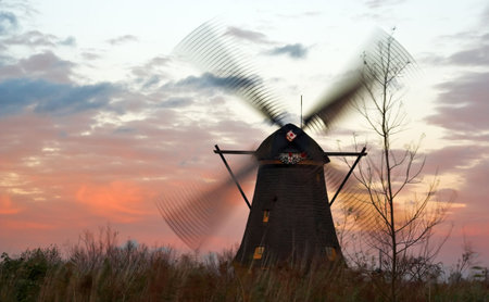 Windmills in Kinderdijk (Netherlands) photographed at windy sunset. The windmill wings and the...