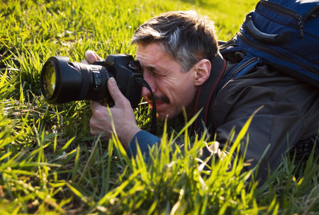 Photographer taking picture while lying on grass in bright sunny day