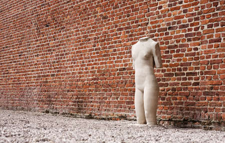 Lonely sculpture standing next to red-brick wallの写真素材