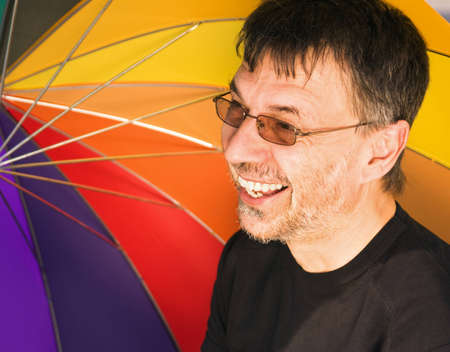 Happy mature man under a colorful umbrellaの写真素材