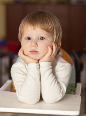 thoughtful blond boy resting elbows on the table