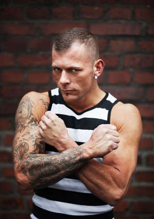 Serious muscular man standing against a brick wall; selective focusの写真素材