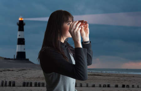 Brunette woman looking via binoculars; lighthouse on backgroundの写真素材