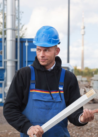 Young manual worker in blue hardhat and workwear holds foldable ruler
