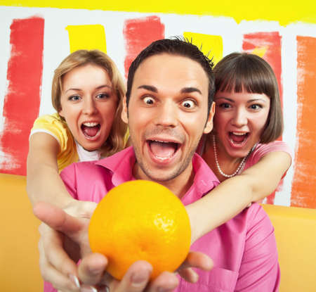 Group of three people is very emotional about an orange; room painted in vivid colorsの写真素材