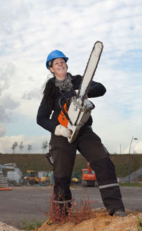 Female worker in workwear and hardhat holds large chainsawの写真素材