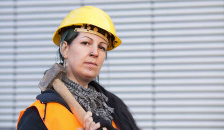 Female worker in workwear and hardhat holds hammerの写真素材