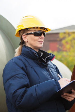Woman in yellow hard hat taking notes while standing in a construction site
