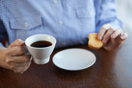 Hands of an elderly woman holding cup of coffee and cookieの写真素材