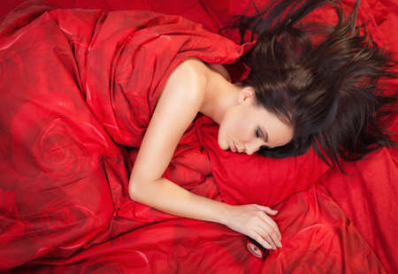 High angle portrait of pretty young woman sleeping on red linenの写真素材