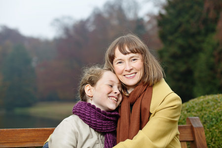 Happy mother and daughter embracing on a bench in an autumn park