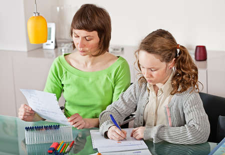 Teenager girl sitting together with her mother and showing her homeworkの写真素材