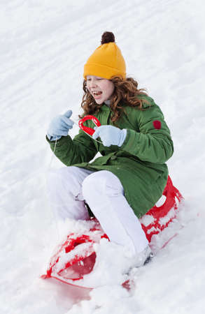 Girl slides down hill on red plastic sledge in a snowy winter parkの写真素材