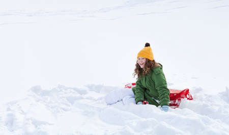Smiling teenager girl with red plastic sledge sitting in snow の写真素材