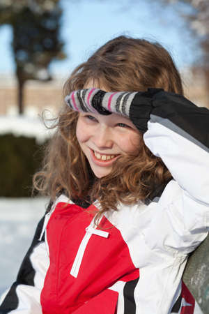 Smiling blond girl in winther cloths sitting on a bench in winter snowy parkの写真素材