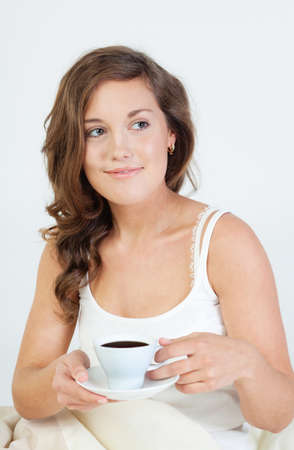 Pretty young woman waken up and having coffee in her bedの写真素材