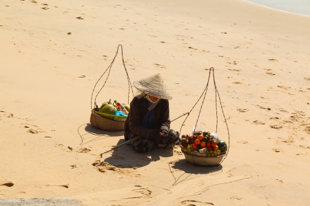 Vietnamese woman in a straw hat on the beach selling fruit and reveals the coconutの写真素材