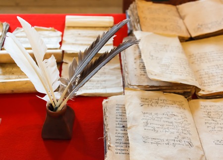 feathers and inkpot with Old books on the red tableclothの写真素材