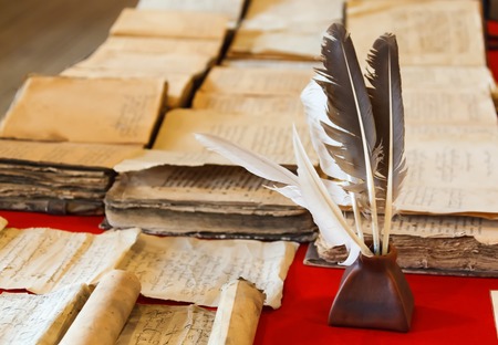 feathers and inkpot with Old books on the red tableclothの写真素材