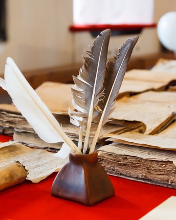 feathers and inkpot with Old books on the red tableclothの写真素材