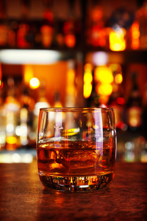 glass of whisky on a dark wooden table with illuminated bar on the backgroundの写真素材