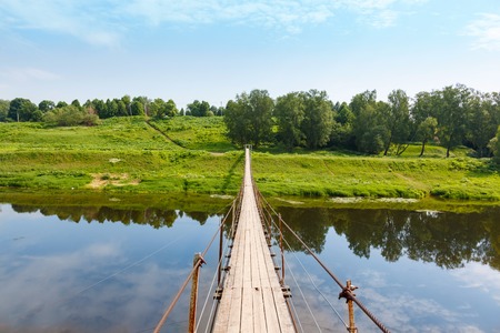 Pedestrian suspension bridge of steel and wood over the river, summer in Russiaの写真素材