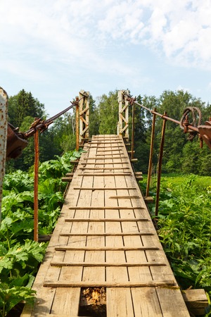 Pedestrian suspension bridge of steel and wood over the river, summer in Russiaの写真素材