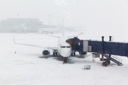 blizzard at the airport and airplane at gate and gangways for the planeの写真素材