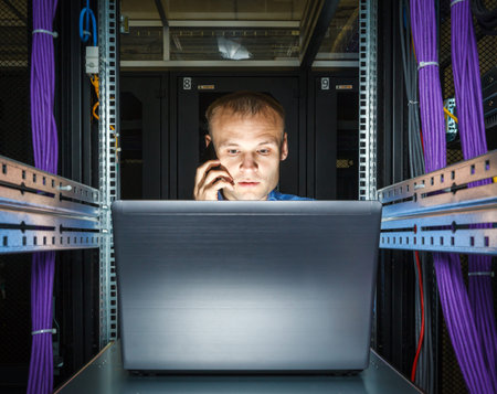 IT Engineer talking on the phone and working on a laptop that is lying in the rack in datacenter