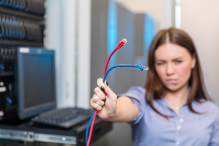 Young engineer and businesswoman with the management console holds two colored patch cords And stands between the server racks in the data centerの写真素材