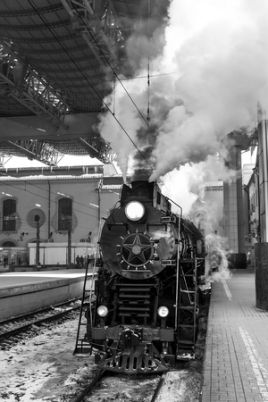 old black steam locomotive in Russia in the winter and electric trains on the background of the Moscow railway station.の写真素材