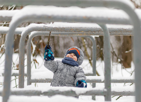 Happy baby boy playing in winter with snow, knocks snow down.の写真素材