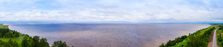 Summer landscape of a lake with a stony shore with a with green grass in the foreground and a blue...