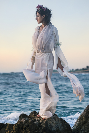 Beautiful woman in a white dress walking along the edge of the beach during a sunset. Horizon lineの写真素材