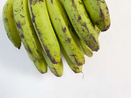 Green banana hanging on the wall of a white buildingの写真素材