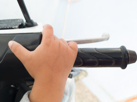 A tan toddler's hand holds a motorbike steering wheelの写真素材